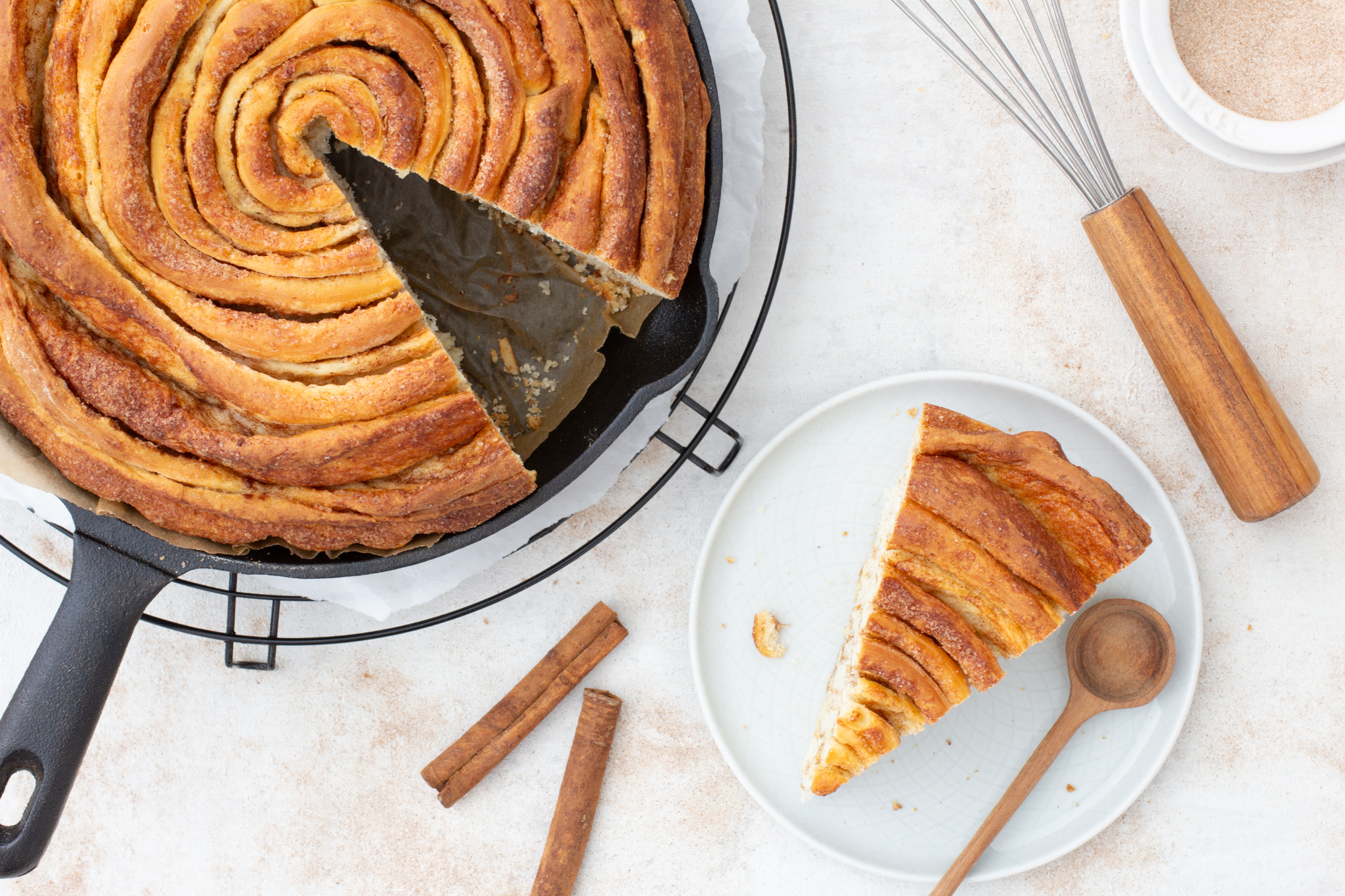 1 Stück Zimtschnecke, angeschnittener Zimtschneckenkuchen, 2 Stangen Zimt und ein Schneebesen
