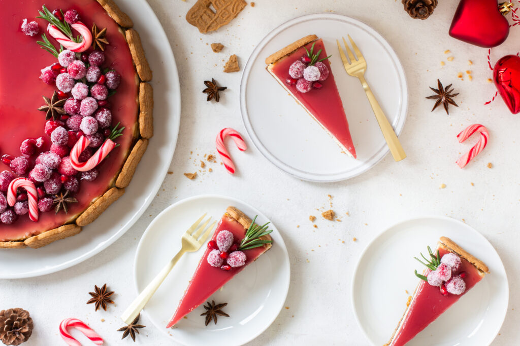 Spekulatius Cheesecake mit einem Granatapfelspiegel und einem opulenten Topping aus kandierten Cranberries, Granatapfelkernen, Sternanis und Rosmarin, von oben fotografiert, 3 Stücke aufgeschnitten