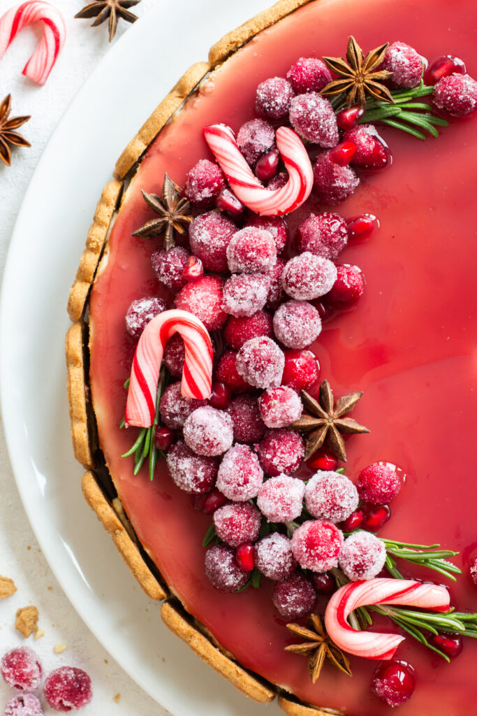 Spekulatius Cheesecake mit einem Granatapfelspiegel und einem opulenten Topping aus kandierten Cranberries, Granatapfelkernen, Sternanis und Rosmarin, als Nahaufnahme von oben fotografiert