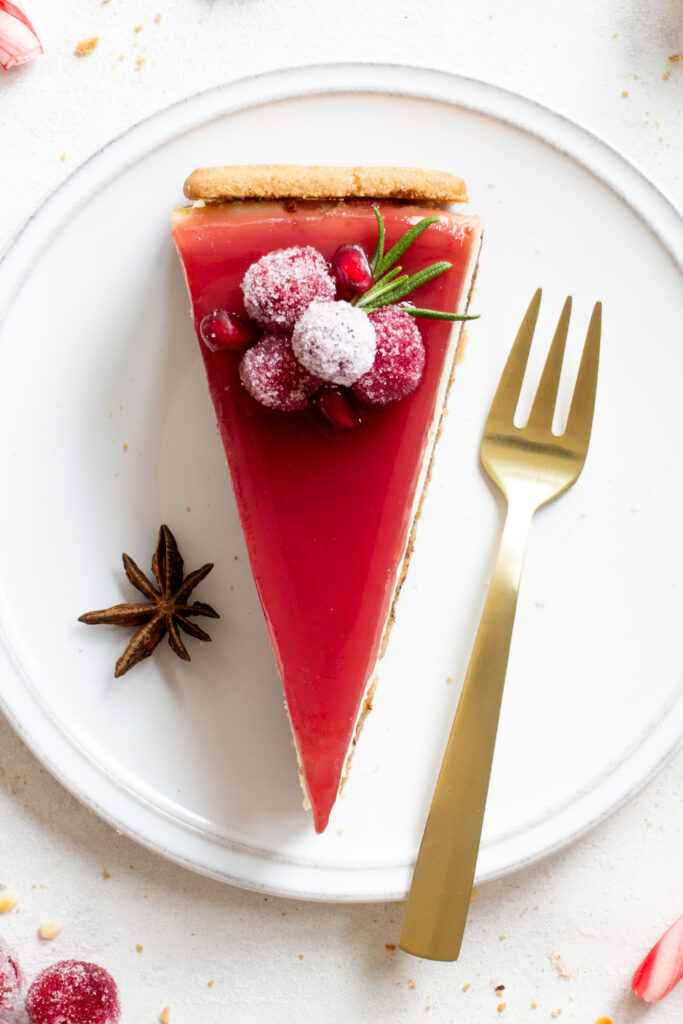 Ein Stück Spekulatius Cheesecake mit einem Granatapfelspiegel und einem Topping aus kandierten Cranberries, Granatapfelkernen, Sternanis und Rosmarin, von oben fotografiert, Nahaufnahme
