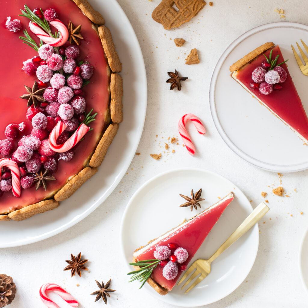 Spekulatius Cheesecake mit einem Granatapfelspiegel und einem opulenten Topping aus kandierten Cranberries, Granatapfelkernen, Sternanis und Rosmarin, von oben fotografiert, 2 Stücke aufgeschnitten