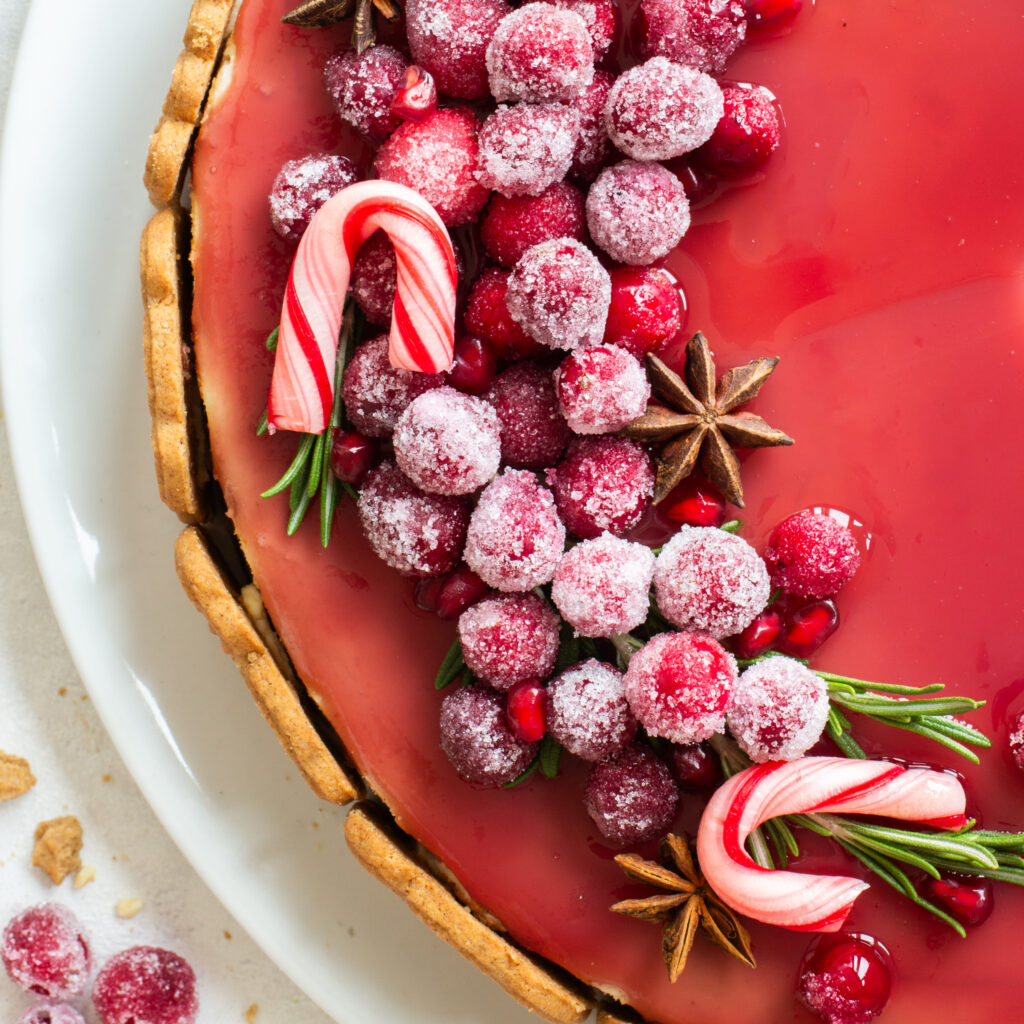 Spekulatius Cheesecake mit einem Granatapfelspiegel und einem opulenten Topping aus kandierten Cranberries, Granatapfelkernen, Sternanis und Rosmarin, von oben fotografiert