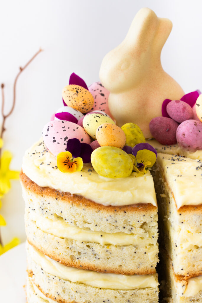 Nahaufnahme der Ostertorten-Deko aus bunten Schokoeiern, Blüten und einem weißen Schokohasen