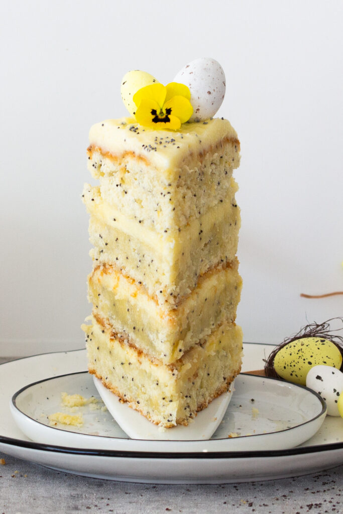 Ein Stück zitronig-frische Ostertorte mit Mohn und farbenfroher Frühlingsdeko on top