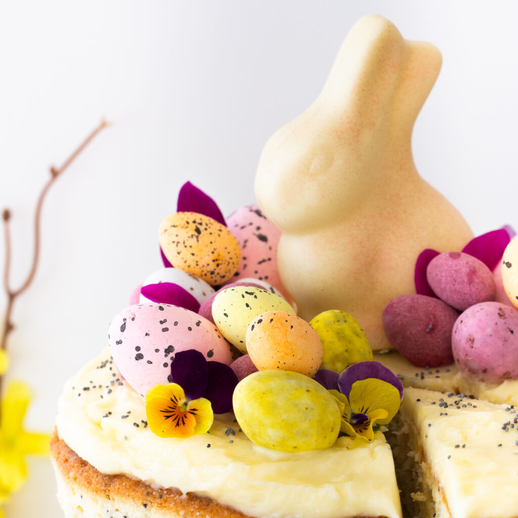 Nahaufnahme der Ostertorten-Deko aus bunten Schokoeiern, Blüten und einem weißen Schokohasen