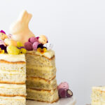 Angeschnittene zitronig-frische 4-schichtige Ostertorte mit Mohn und farbenfroher Frühlingsdeko
