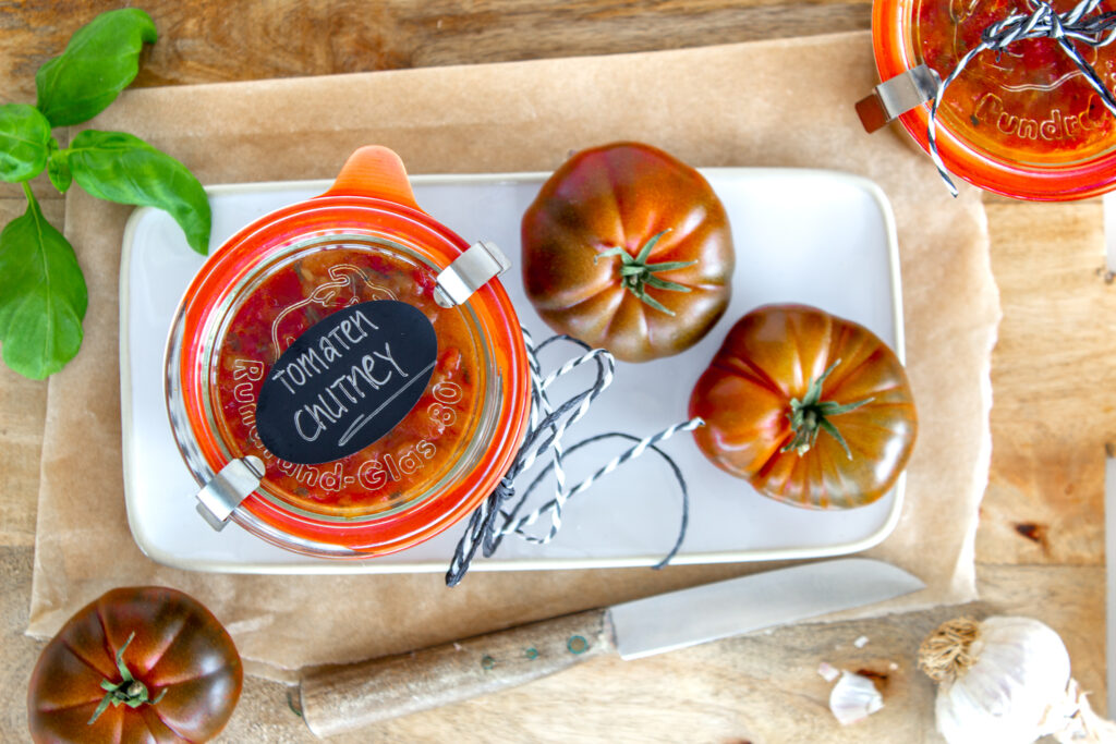 Ein Glas selbstgemachtes Tomaten-Chutney als Geschenk verpackt auf einem Teller, nebenan liegen zwei Tomaten