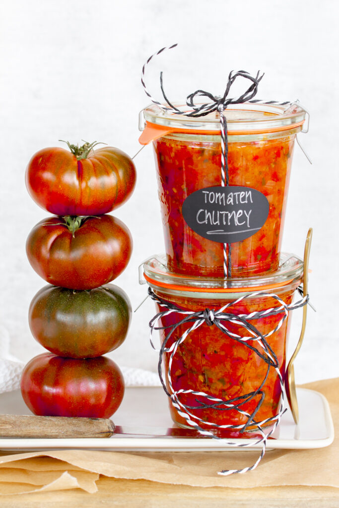 Ein Glas selbstgemachtes Tomaten-Chutney auf einem Teller mit Tomaten