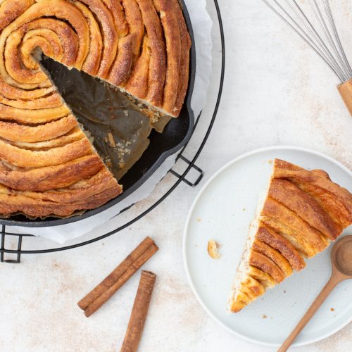 1 Stück Zimtschnecke, angeschnittener Zimtschneckenkuchen, 2 Stangen Zimt und ein Schneebesen